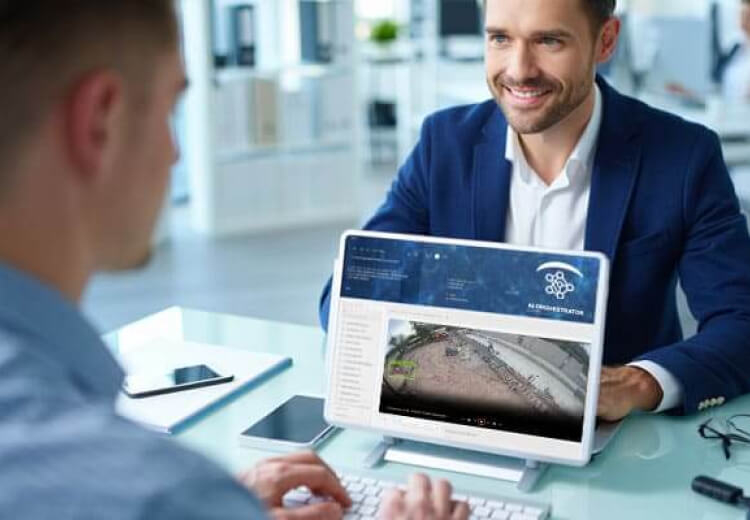 Consultor tecnológico explicando soluciones de videovigilancia con inteligencia artificial a un cliente, frente a una pantalla con gráficos de análisis en tiempo real.