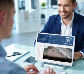 Consultor tecnológico explicando soluciones de videovigilancia con inteligencia artificial a un cliente, frente a una pantalla con gráficos de análisis en tiempo real.